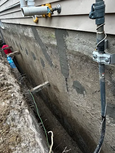 Waterproofing worker working in a narrow exterior foundation trench