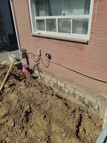 Perforated drainage pipe being installed beside a foundation wall