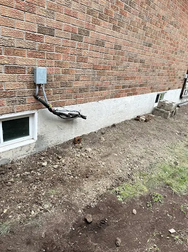 Worker applying a black waterproof coating to an excavated foundation wall